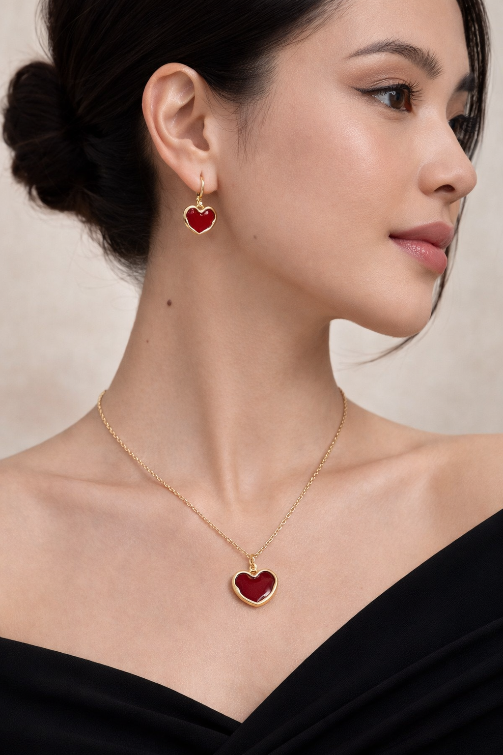 Woman wearing a gold necklace and red heart-shaped earrings against a neutral background