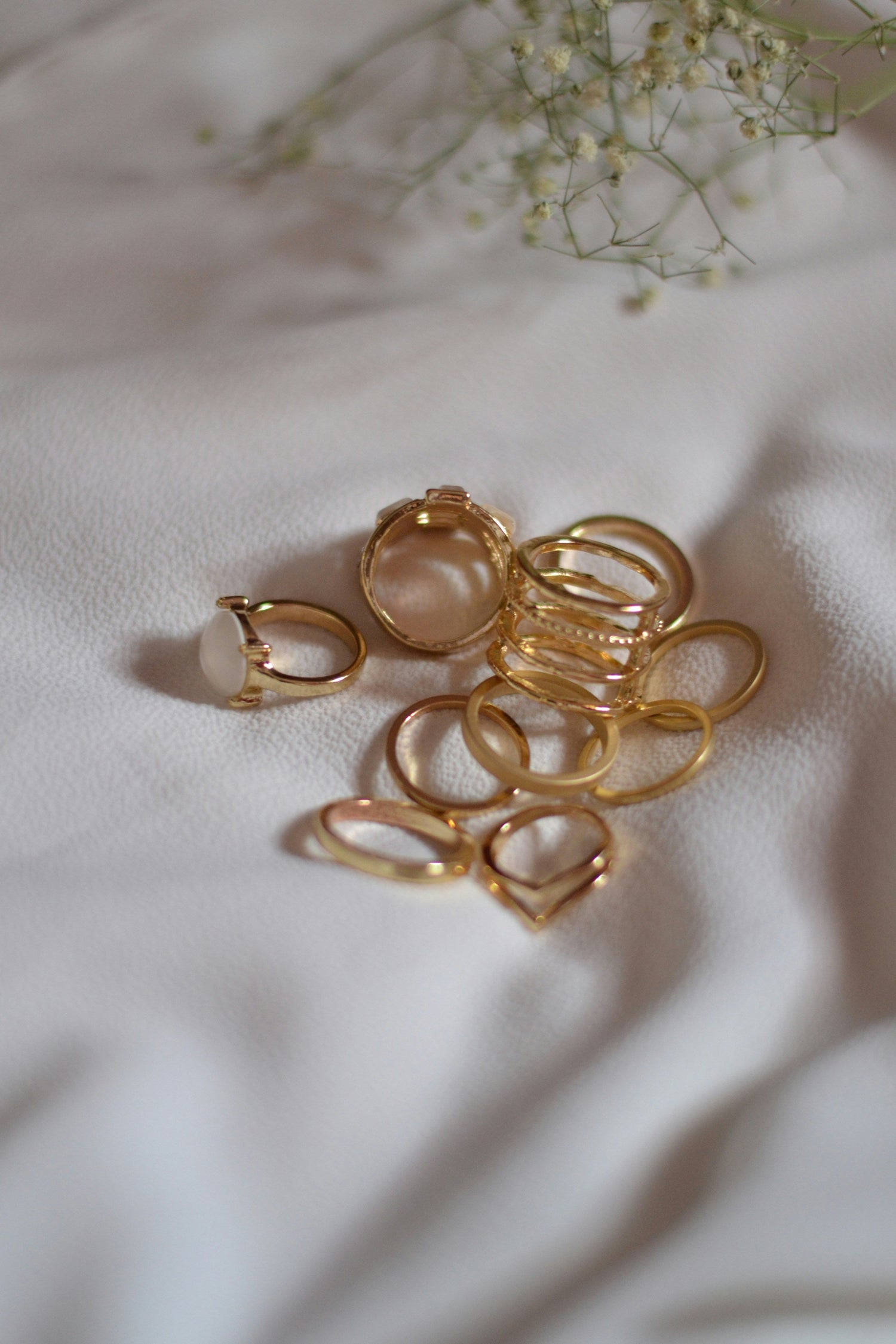 Flat lay of gold-plated earrings and rings on white fabric – waterproof, tarnish-free jewelry by Nyaara
