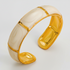 A wide cuff bracelet featuring alternating curved panels of glossy gold and milky white enamel, photographed on a light gray background.
