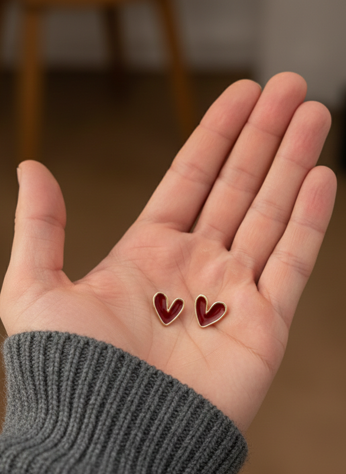 Two red heart-shaped earrings held in the palm of a hand.