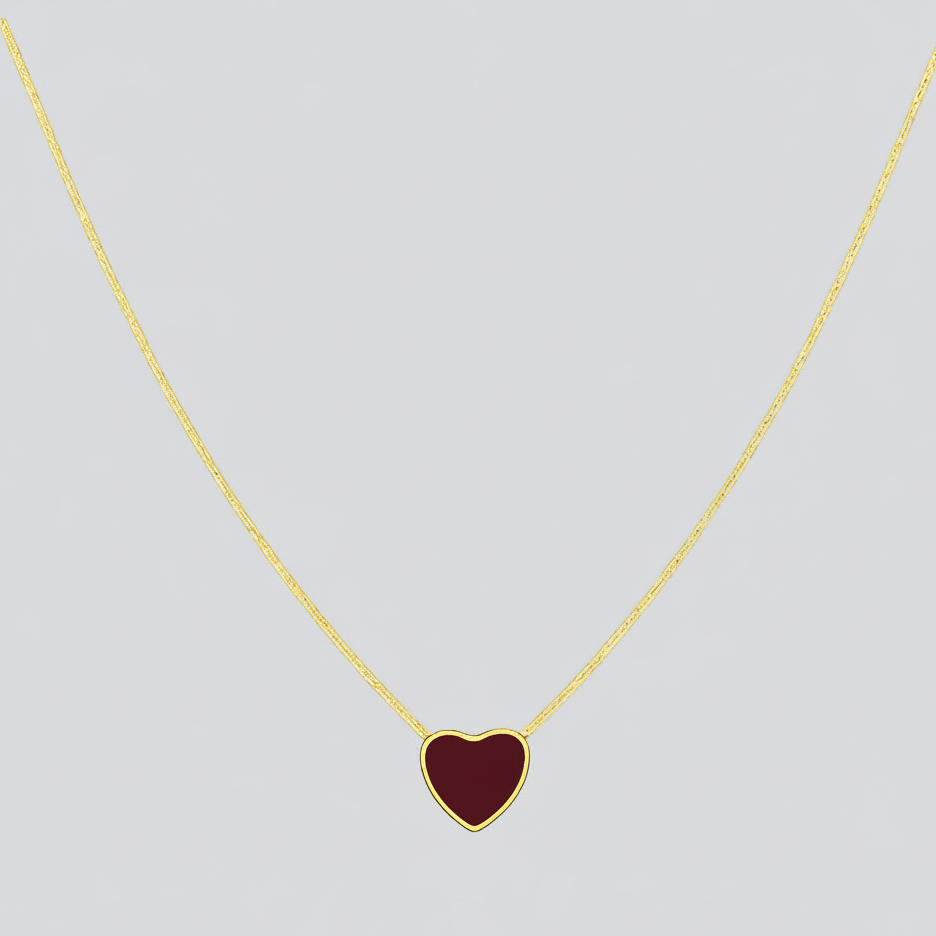 Gold necklace with a red heart pendant on a light gray background