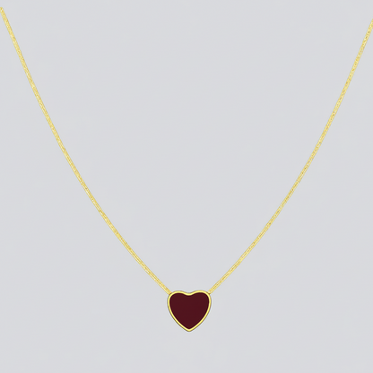 Gold necklace with a red heart pendant on a light gray background