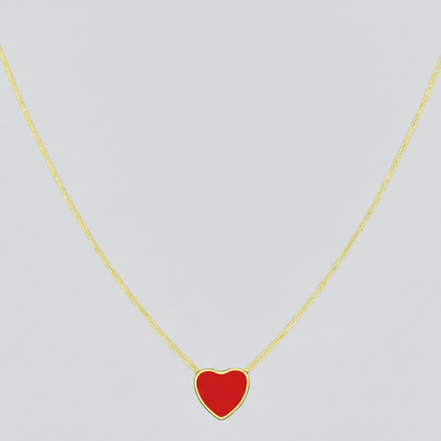 Gold necklace with a red heart pendant on a light gray background