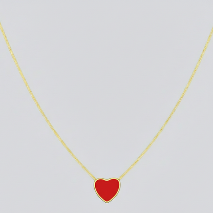 Gold necklace with a red heart pendant on a light gray background